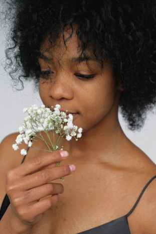 close up portrait photo of woman in black spaghetti strap top smelling white petaled flower